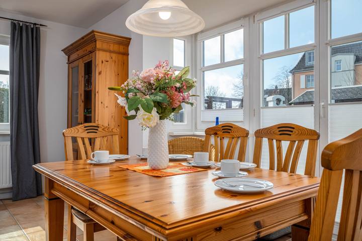 Gedeckter Holz-Esstisch mit Blumenstrauß vor großen Fenstern
